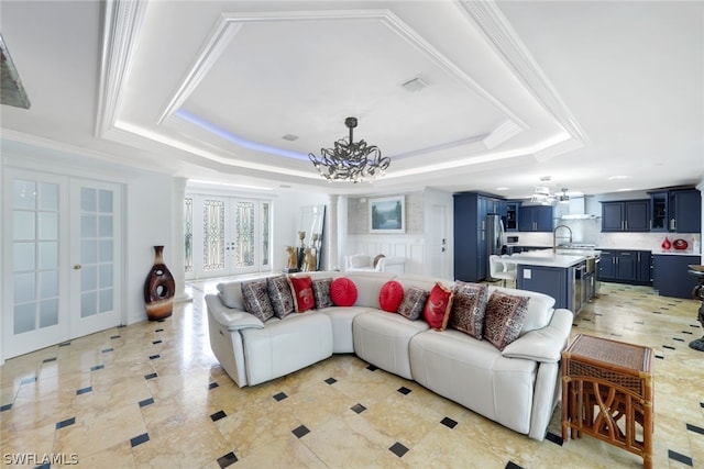 living room with a raised ceiling, sink, crown molding, french doors, and a chandelier