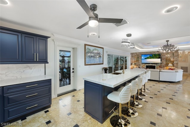 kitchen featuring a kitchen bar, crown molding, a kitchen island with sink, blue cabinets, and ceiling fan with notable chandelier