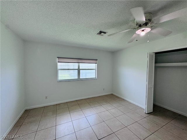 unfurnished bedroom with ceiling fan, a closet, light tile patterned floors, and a textured ceiling