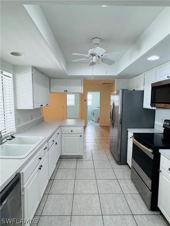 kitchen with white cabinetry, sink, a tray ceiling, light tile patterned floors, and appliances with stainless steel finishes