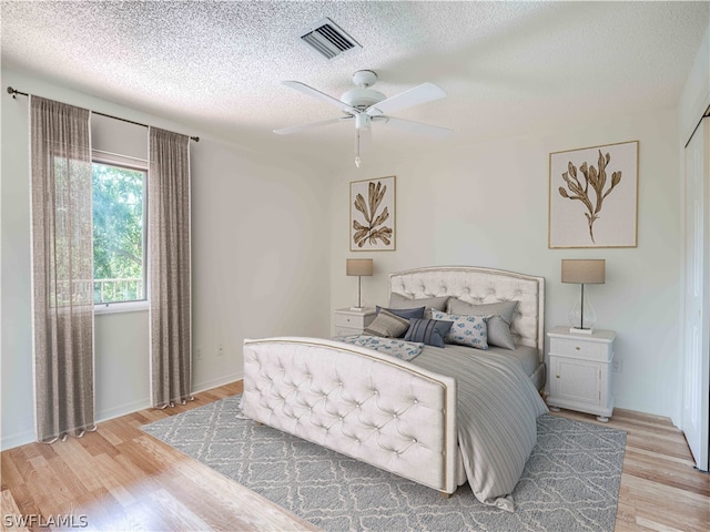 bedroom with a textured ceiling, light hardwood / wood-style flooring, and ceiling fan