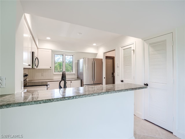 kitchen featuring white cabinetry, kitchen peninsula, appliances with stainless steel finishes, stone countertops, and decorative backsplash