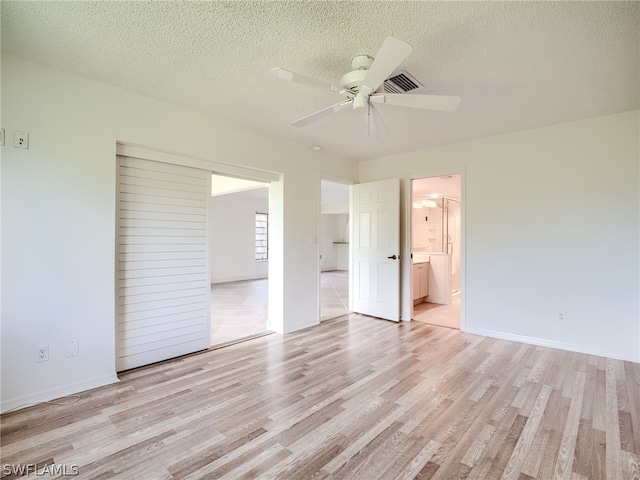 unfurnished bedroom with light wood-type flooring, ceiling fan, connected bathroom, and a textured ceiling