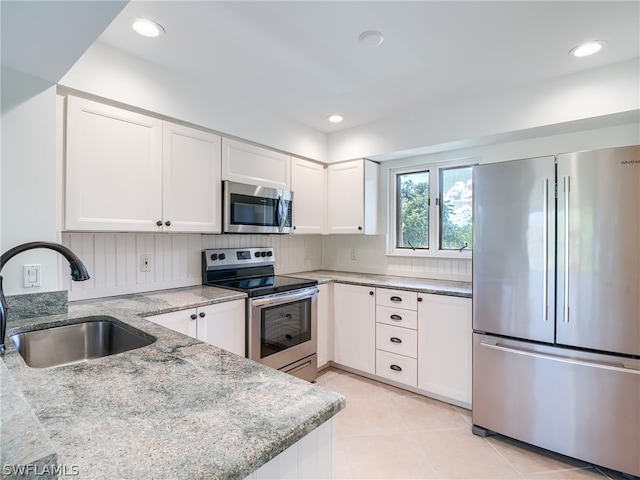 kitchen with light tile patterned flooring, white cabinets, stainless steel appliances, decorative backsplash, and sink