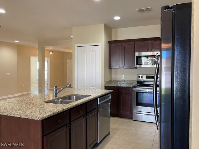 kitchen with sink, light stone counters, a kitchen island with sink, light tile patterned floors, and appliances with stainless steel finishes