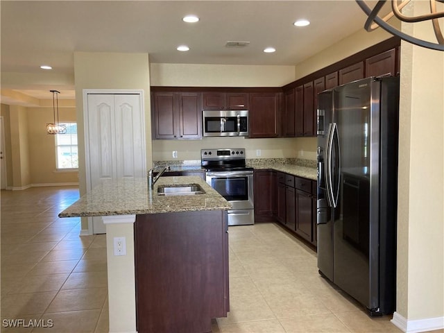 kitchen with sink, appliances with stainless steel finishes, light stone countertops, an island with sink, and decorative light fixtures