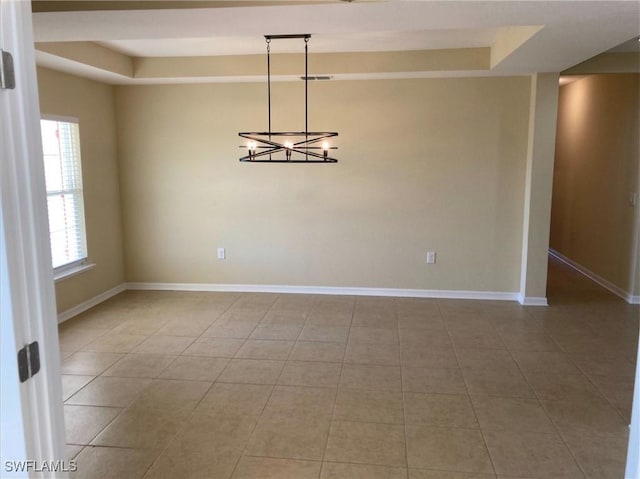 tiled spare room featuring a raised ceiling and a notable chandelier