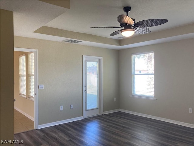 empty room with a raised ceiling, ceiling fan, and dark hardwood / wood-style flooring