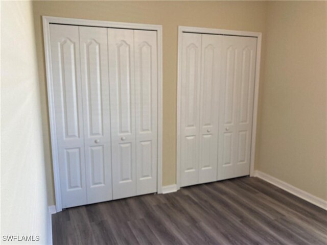 unfurnished bedroom featuring dark hardwood / wood-style floors and two closets