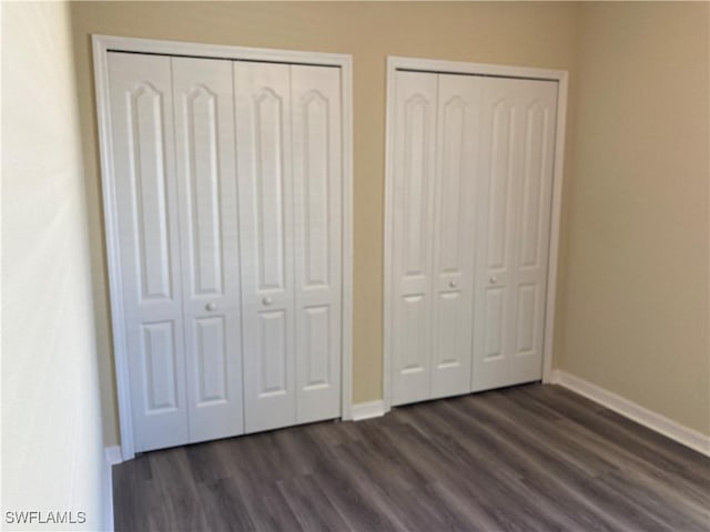 unfurnished bedroom with dark wood-type flooring and multiple closets