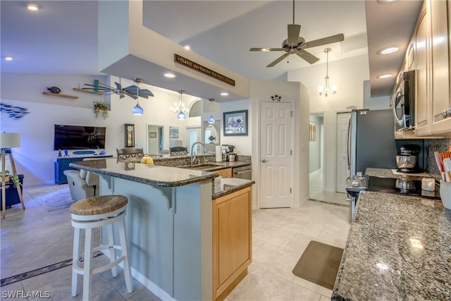 kitchen featuring a breakfast bar area, appliances with stainless steel finishes, dark stone counters, sink, and ceiling fan with notable chandelier