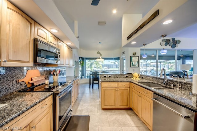 kitchen featuring dark stone countertops, appliances with stainless steel finishes, light brown cabinetry, sink, and decorative light fixtures