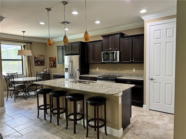 kitchen with sink, an island with sink, appliances with stainless steel finishes, decorative light fixtures, and a kitchen bar