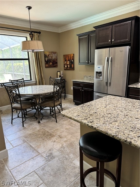 kitchen featuring hanging light fixtures, stainless steel fridge, light stone countertops, ornamental molding, and dark brown cabinetry