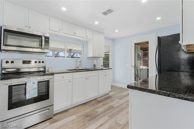 kitchen with sink, appliances with stainless steel finishes, white cabinets, dark stone counters, and light wood-type flooring