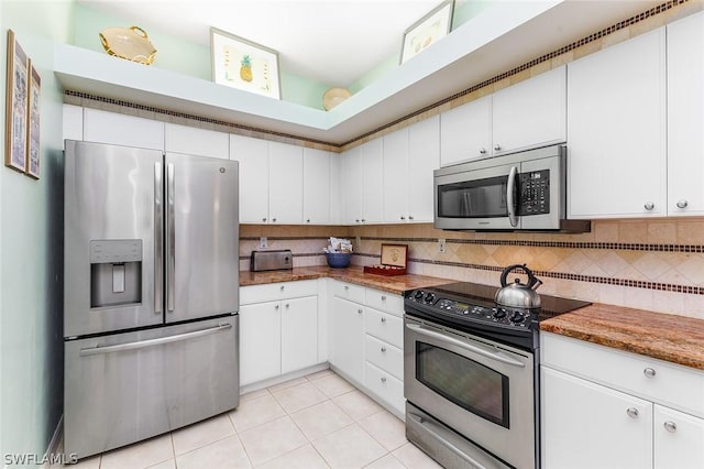 kitchen with light tile patterned floors, white cabinetry, appliances with stainless steel finishes, tasteful backsplash, and stone countertops