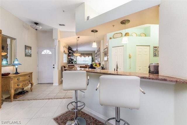 kitchen with a towering ceiling, a kitchen bar, hanging light fixtures, kitchen peninsula, and light tile patterned floors