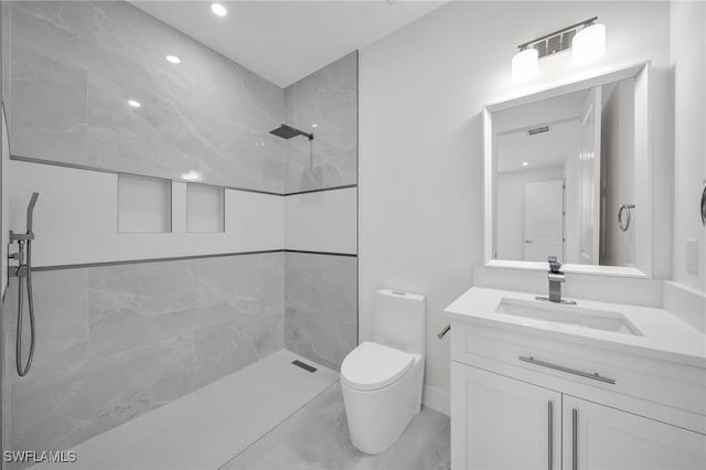 bathroom with tile patterned flooring, toilet, tiled shower, and vanity