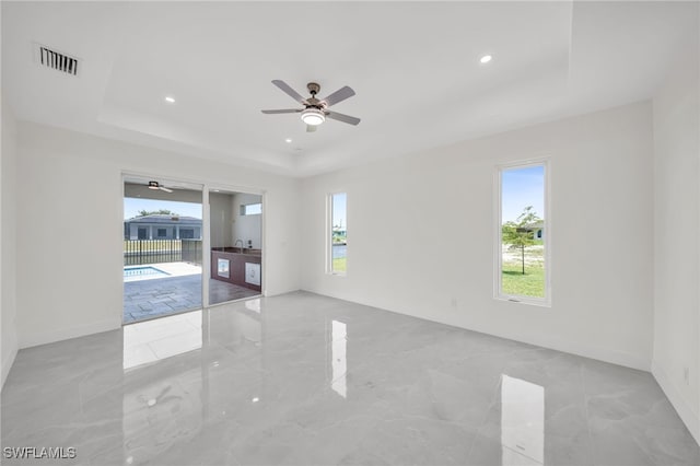 empty room with ceiling fan, a tray ceiling, and light tile patterned floors