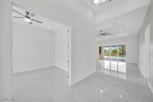 tiled empty room with ceiling fan and a raised ceiling