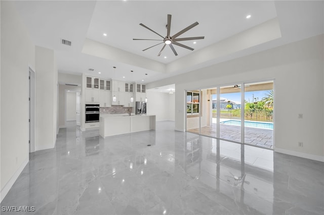 unfurnished living room with a tray ceiling, ceiling fan, light tile patterned flooring, and sink