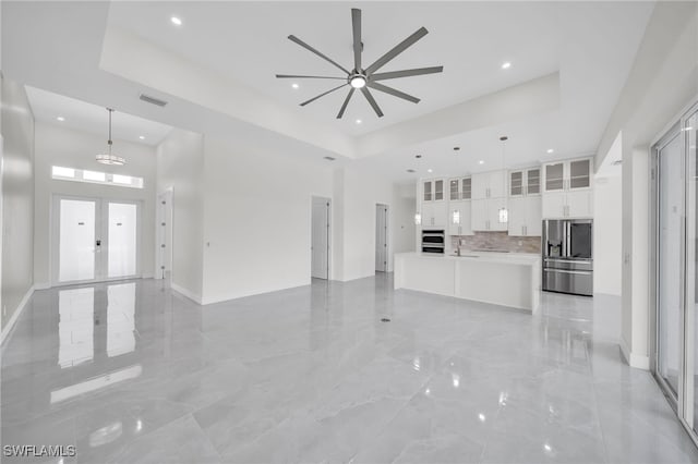 unfurnished living room with a towering ceiling, french doors, a tray ceiling, and light tile patterned flooring