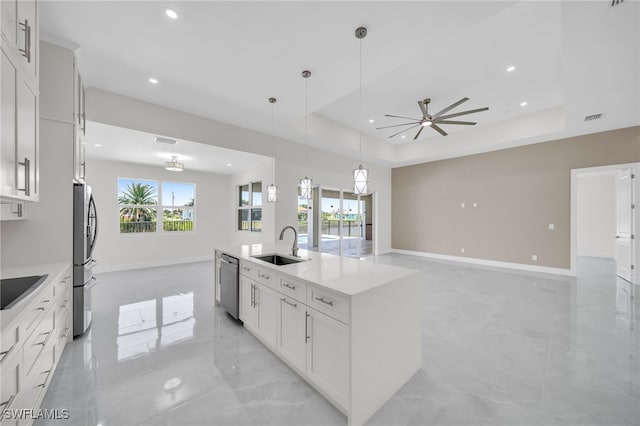 kitchen with appliances with stainless steel finishes, a center island with sink, light tile patterned floors, a tray ceiling, and ceiling fan