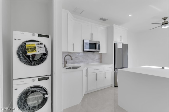 kitchen with sink, appliances with stainless steel finishes, stacked washer / dryer, ceiling fan, and white cabinetry