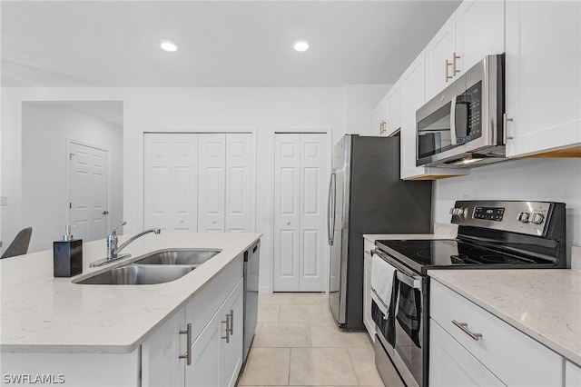 kitchen featuring white cabinets, appliances with stainless steel finishes, sink, light stone counters, and a center island with sink