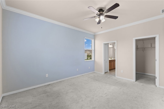 unfurnished bedroom with a spacious closet, connected bathroom, light colored carpet, crown molding, and ceiling fan