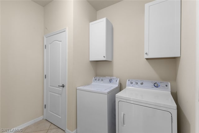 clothes washing area featuring cabinets, light tile patterned floors, and washing machine and clothes dryer