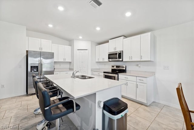 kitchen featuring stainless steel appliances, a breakfast bar, a center island with sink, and white cabinets