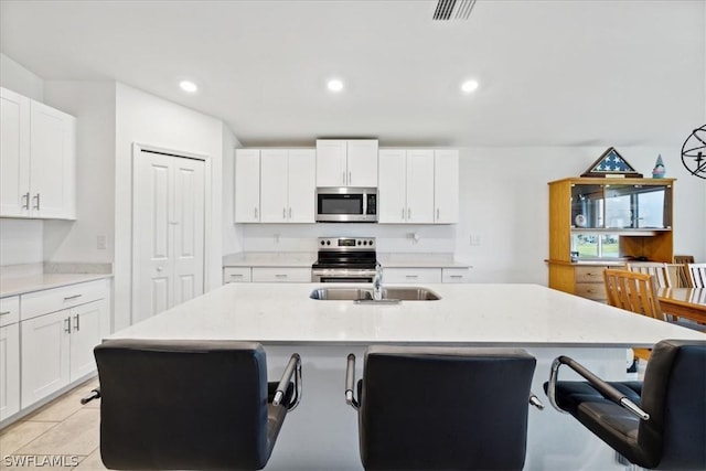 kitchen with sink, a kitchen island with sink, white cabinetry, stainless steel appliances, and light stone countertops