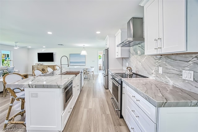 kitchen featuring light stone countertops, appliances with stainless steel finishes, wall chimney range hood, white cabinetry, and a large island