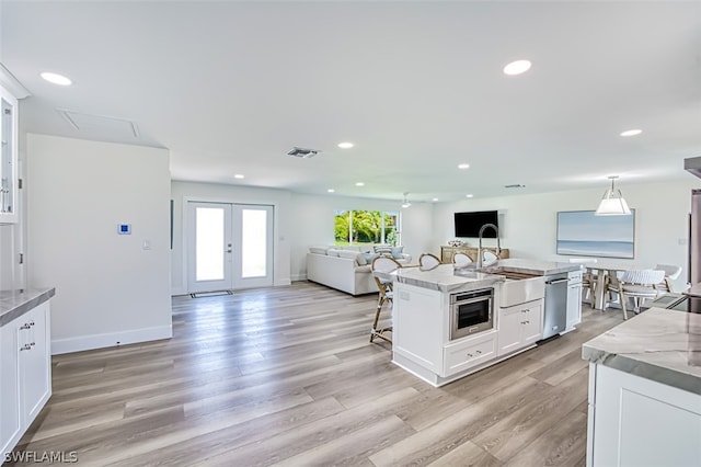 kitchen with white cabinets, a center island with sink, sink, light stone counters, and a breakfast bar area