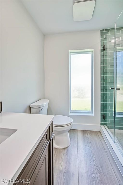 bathroom with a shower with door, vanity, hardwood / wood-style floors, and toilet