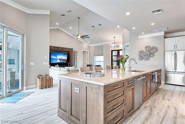 kitchen featuring sink, light stone counters, an island with sink, ceiling fan with notable chandelier, and appliances with stainless steel finishes