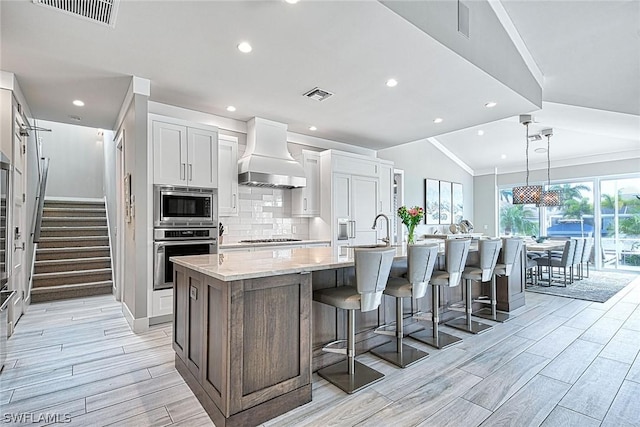 kitchen with premium range hood, stainless steel appliances, an island with sink, tasteful backsplash, and white cabinetry