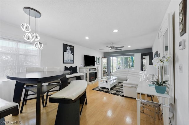 living room with ceiling fan, light wood-type flooring, and a textured ceiling