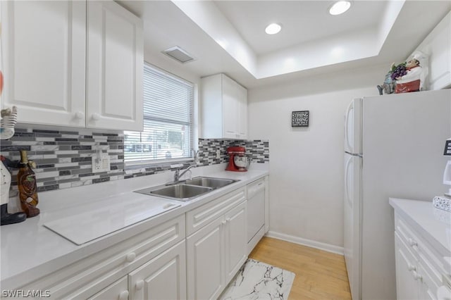 kitchen with white cabinets, a raised ceiling, sink, light hardwood / wood-style floors, and white fridge