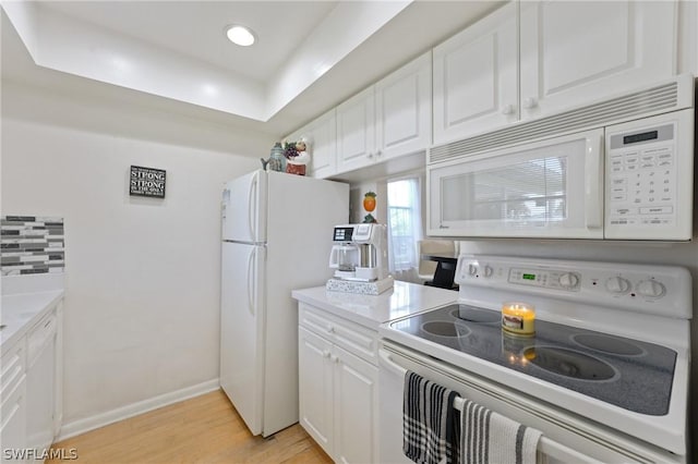 kitchen with tasteful backsplash, a raised ceiling, white appliances, white cabinets, and light wood-type flooring