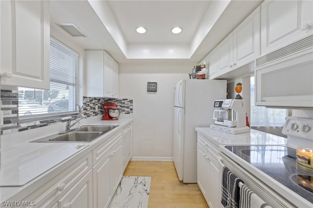 kitchen with white cabinetry, sink, a raised ceiling, light hardwood / wood-style floors, and white appliances