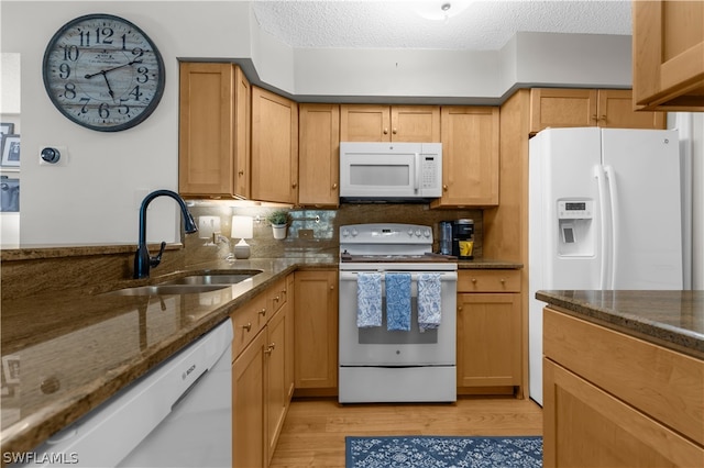 kitchen with sink, a textured ceiling, white appliances, and dark stone counters