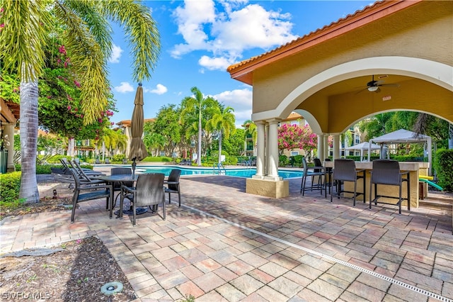 view of patio with a community pool, a gazebo, ceiling fan, and exterior bar