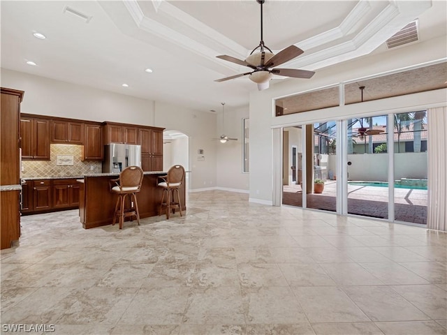 kitchen with tasteful backsplash, a center island, a raised ceiling, a kitchen breakfast bar, and stainless steel fridge with ice dispenser