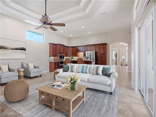 living room featuring ceiling fan, crown molding, a towering ceiling, and a tray ceiling