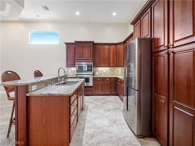 kitchen with stainless steel appliances, tasteful backsplash, sink, a kitchen island with sink, and a breakfast bar