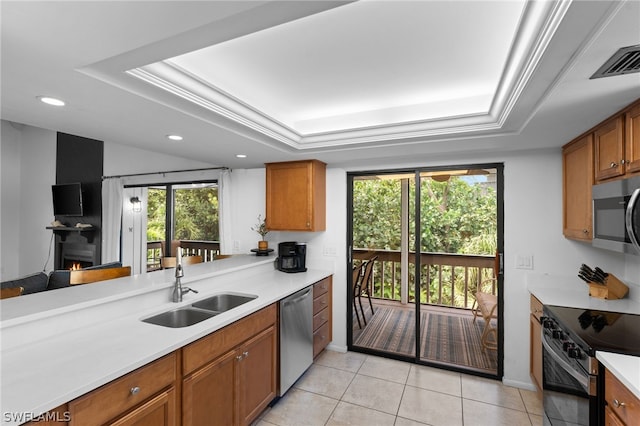 kitchen with sink, a raised ceiling, appliances with stainless steel finishes, light tile patterned flooring, and ornamental molding