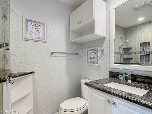 bathroom with vanity, toilet, and tiled shower