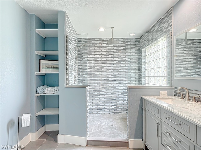 bathroom featuring a textured ceiling, vanity, tile patterned floors, and a tile shower